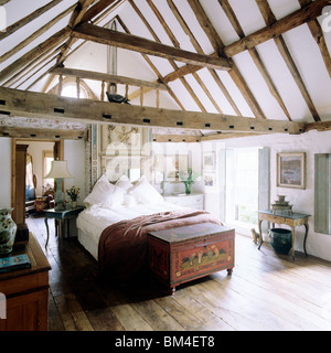 Country bedroom with pitched ceiling and beams with wooden floor and antique chest Stock Photo