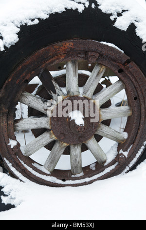 Snow covers an abandoned tractor wooden wagon wheel hub from an ancient vehicle on a farm in Finland Stock Photo