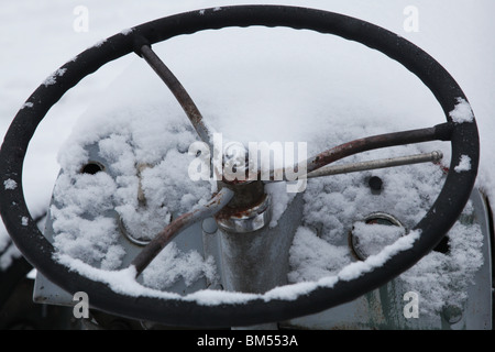 Snow covers a steering wheel on an abandoned antique Ford tractor on a farm in Finland Stock Photo