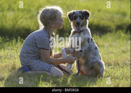 Australian Shepherd (Canis lupus familiaris). Young girl sitting next to young dog on a meadow. Stock Photo