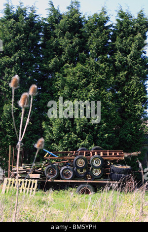 a broken trailer with rusty old trailers stacked on top, in front of conifers in the countryside on a sunny day Stock Photo