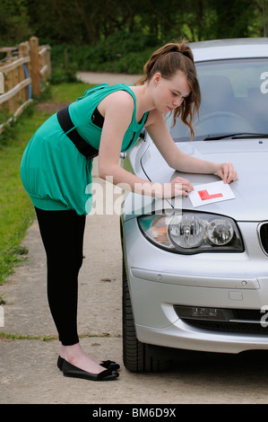 Learner driver putting her L plate onto the bonnet of her car Stock Photo
