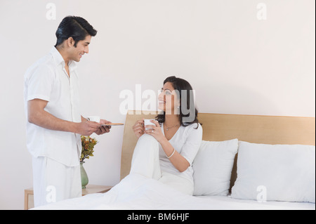Man giving tea to her wife sitting on the bed Stock Photo