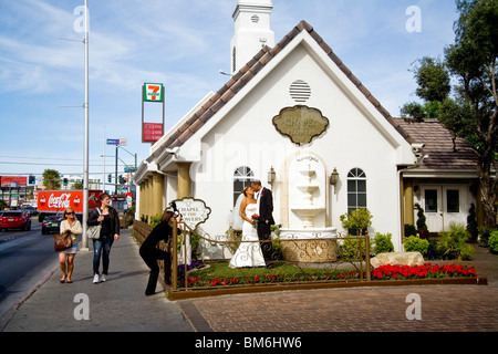 Passersby glance idly as a newly-married couple kiss for professional photographer after the ceremony at a gaudy wedding chapel. Stock Photo