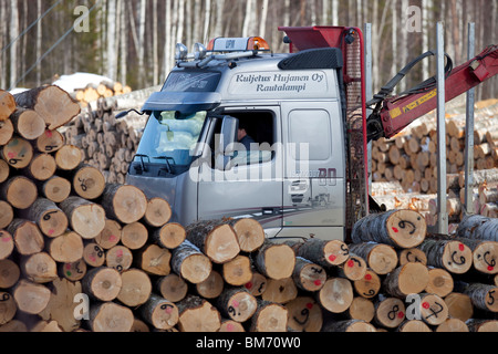 Finnish logging truck and driver driving between log piles in log yard , Finland Stock Photo