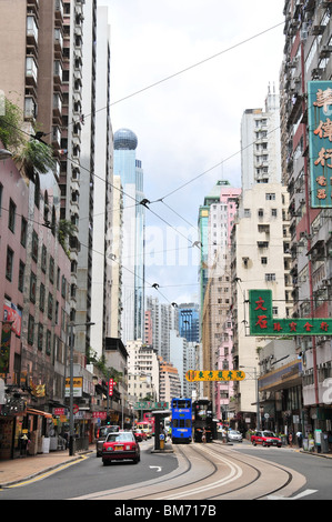 Two trams, in the middle of the road, at the Des Voeux Road West Tram Stop, looking west through a skyscraper canyon, Hong Kong Stock Photo