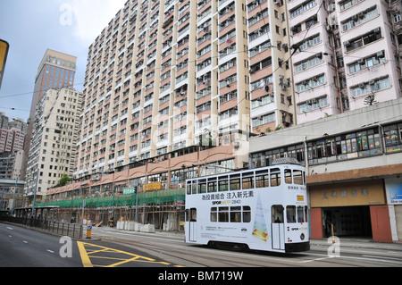 Tram, travelling along Des Voeux Road West, past apartments with bamboo scaffolding, Kennedy Town, Hong Kong, China Stock Photo