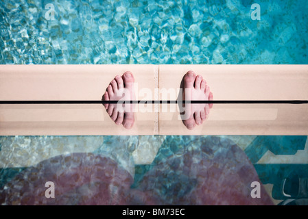 someones feet on the edge of a swimming pool against glass with a reflection making twin feet Stock Photo