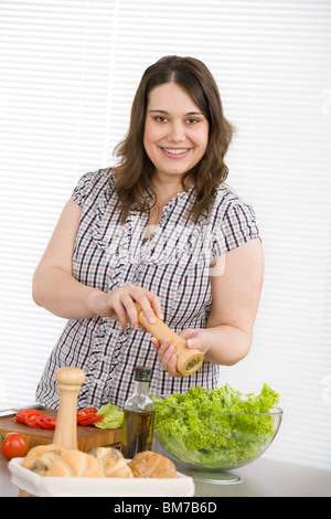 Cook - Plus size happy woman preparing vegetable salad with lettuce in modern kitchen Stock Photo