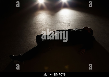 A man lying on the ground in front of a car at night Stock Photo