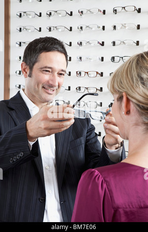 An optician holding up glasses to a customer in an eyewear store Stock Photo