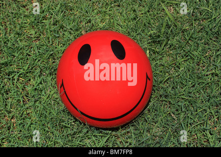 RED SMILEY FACE BALL LAYING ON GRASS  HORIZONTAL  BDA11472 Stock Photo