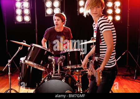A man playing drums and a woman playing guitar performing on stage in a rock band Stock Photo