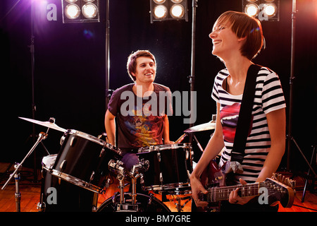 A man playing drums and a woman playing guitar in a rock band performing on stage Stock Photo