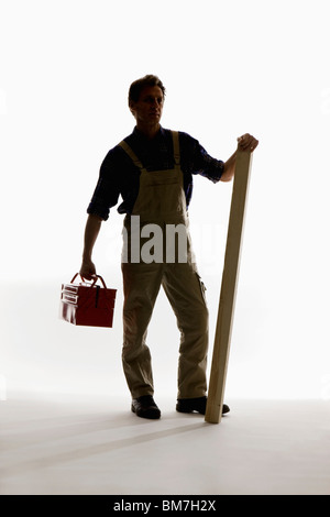 A construction worker holding a toolbox and plank Stock Photo