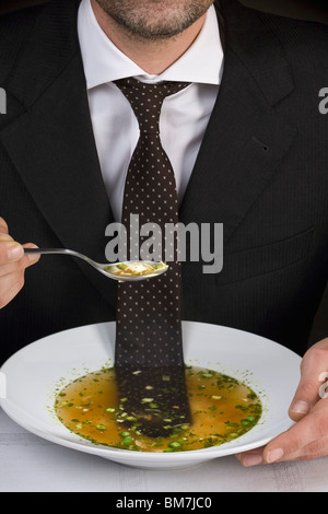 Man sitting at table with tie floating in bowl of soup Stock Photo