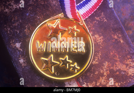 Close up of gold plastic badge on red white and blue ribbon stating Winner lying in warm light on rusty tin lid Stock Photo