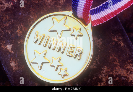Close up of gold plastic badge on red white and blue ribbon stating Winner lying on rusty tin lid Stock Photo