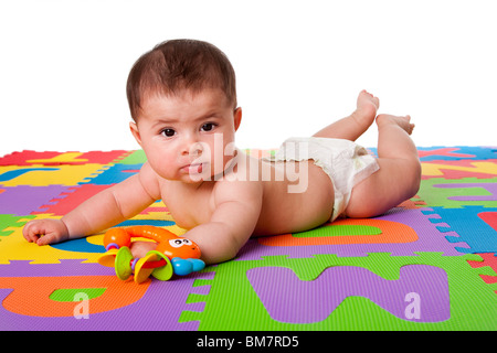 Beautiful cute happy Caucasian Hispanic baby laying on belly on a colorful padded floor tiles with alphabet letters and a toy. Stock Photo