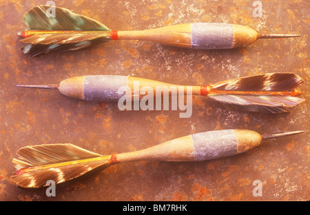 Set of three old dartboard darts made from wood metal lead and feathers lying on rusty metal sheet in warm light Stock Photo