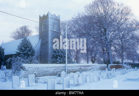 Archetypal English thatched flint church and churchyard with Common beech trees under covering of snow Stock Photo