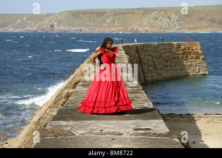 African Woman with Dreadlocks, Wearing a Red Dress, Standing on Quay by the Sea.