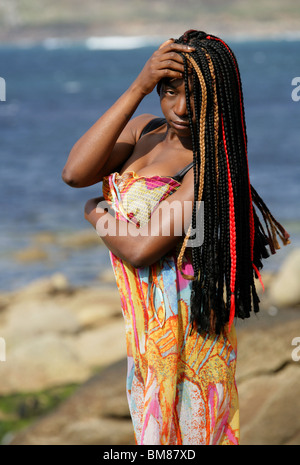 African Woman with Dreadlocks, and Wearing a Colourful Dress, Standing by the Sea.