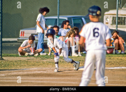 Little league baseball player tags base in hopes of heading home as pitcher thinks Stock Photo
