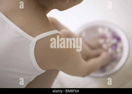 Young woman soaking feet and hands in bowl of water with flower petals Stock Photo