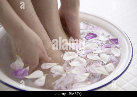 Young woman soaking feet and hands in bowl of water with flower petals, close up Stock Photo