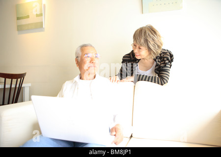 Mature woman talking to senior man using laptop on sofa Stock Photo