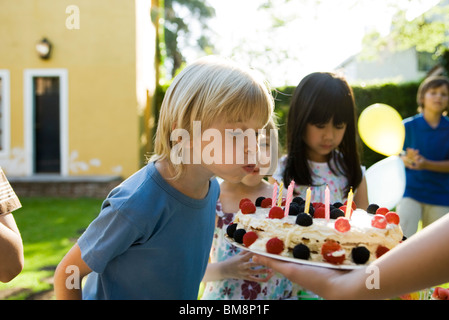 Boy blowing out candles on birthday cake at outdoor birthday party Stock Photo