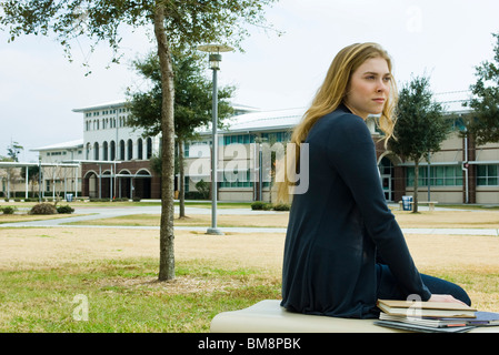 Female student sitting on bench on school campus Stock Photo