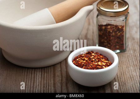 Crushed Chillies In A White Dish, With A Mortar and Pestle and Spice Jar, On A Wooden Kitchen Table Stock Photo