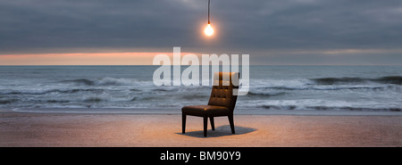 Light bulb illuminated over chair on beach at sunset Stock Photo