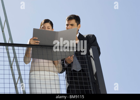 Business associates reading document together on balcony Stock Photo