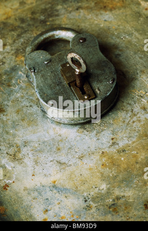 Old fashioned rusty padlock with key over a grungy background Stock Photo