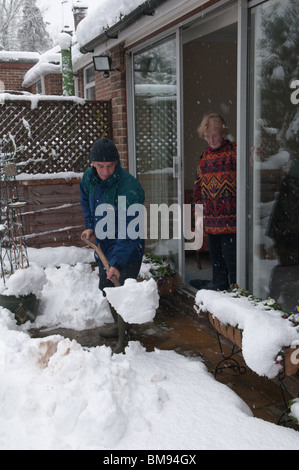 neighbour or relative helping elderly person by clearing snow from path outside of the house Stock Photo