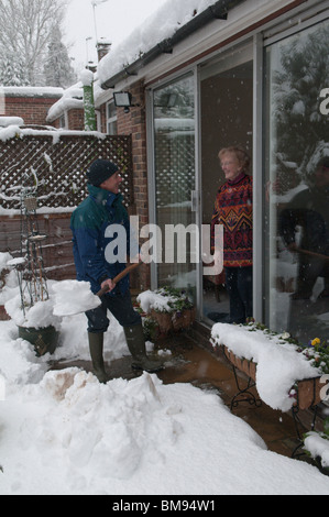 neighbour or relative helping elderly person by clearing snow from path outside of the house Stock Photo