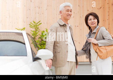 Senior couple standing by car, smiling and looking away Stock Photo