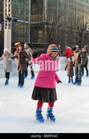 A woman skating at Canary Wharf ice rink, London Docklands, UK. IMPT: Image has limited focus on the pink coat lady. Others blur Stock Photo