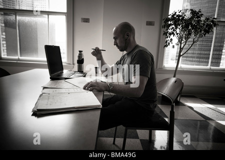 Balding young man working on his laptop computer in the dining area at his college. Stock Photo