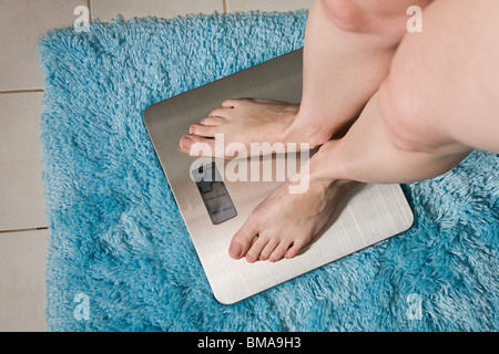 Young woman weighing herself on bathroom scales Stock Photo