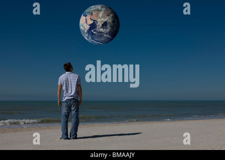 Man on beach looking up at planet earth orbiting overhead Stock Photo