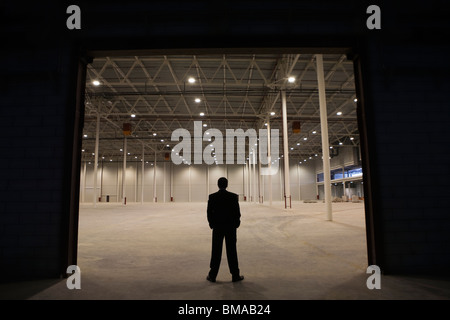 Man stands with hands in pockets at warehouse entrance Stock Photo