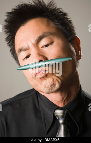 Businessman Holding Pen Between Nose and Puckered Lips Stock Photo