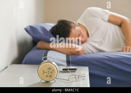 Man Sleeping in Bed with Alarm Clock on Bedside Table Stock Photo