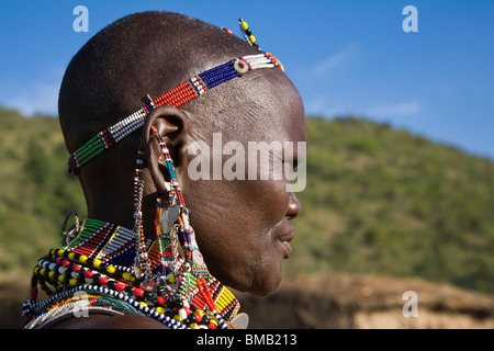 side view Close-up portrait of mature Masai female in traditional tribal costume beaded earrings, necklace Maasai Mara Kenya Stock Photo