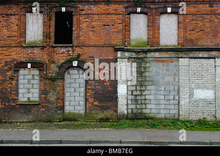 Abandoned house and shop with bricked up windows and doors in a street in Belfast Stock Photo