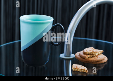 Green/black mug and biscuits on glass side table Stock Photo